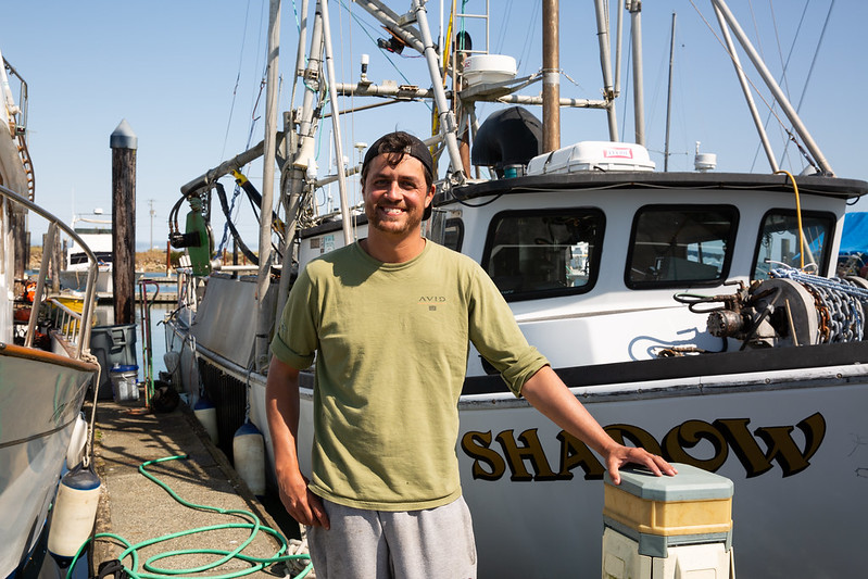 A fisherman stands in front of his boat