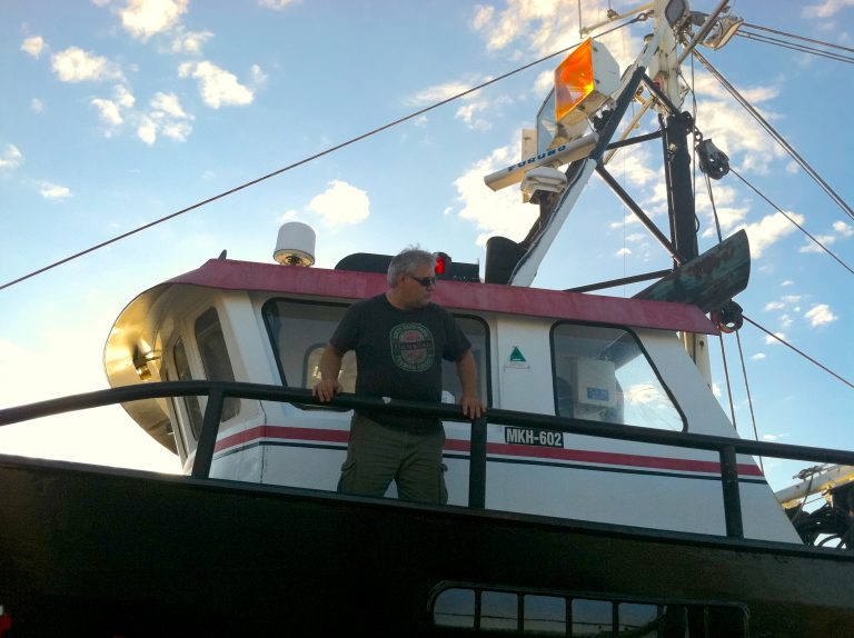 Dave Sones stands on the deck of his ship looking out over a railing.