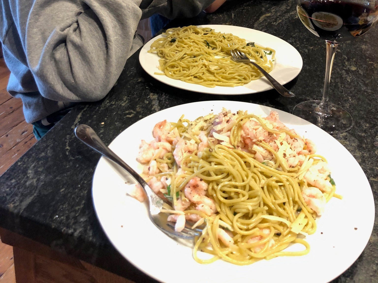 Two plates with spaghetti and shrimp on a dark table.