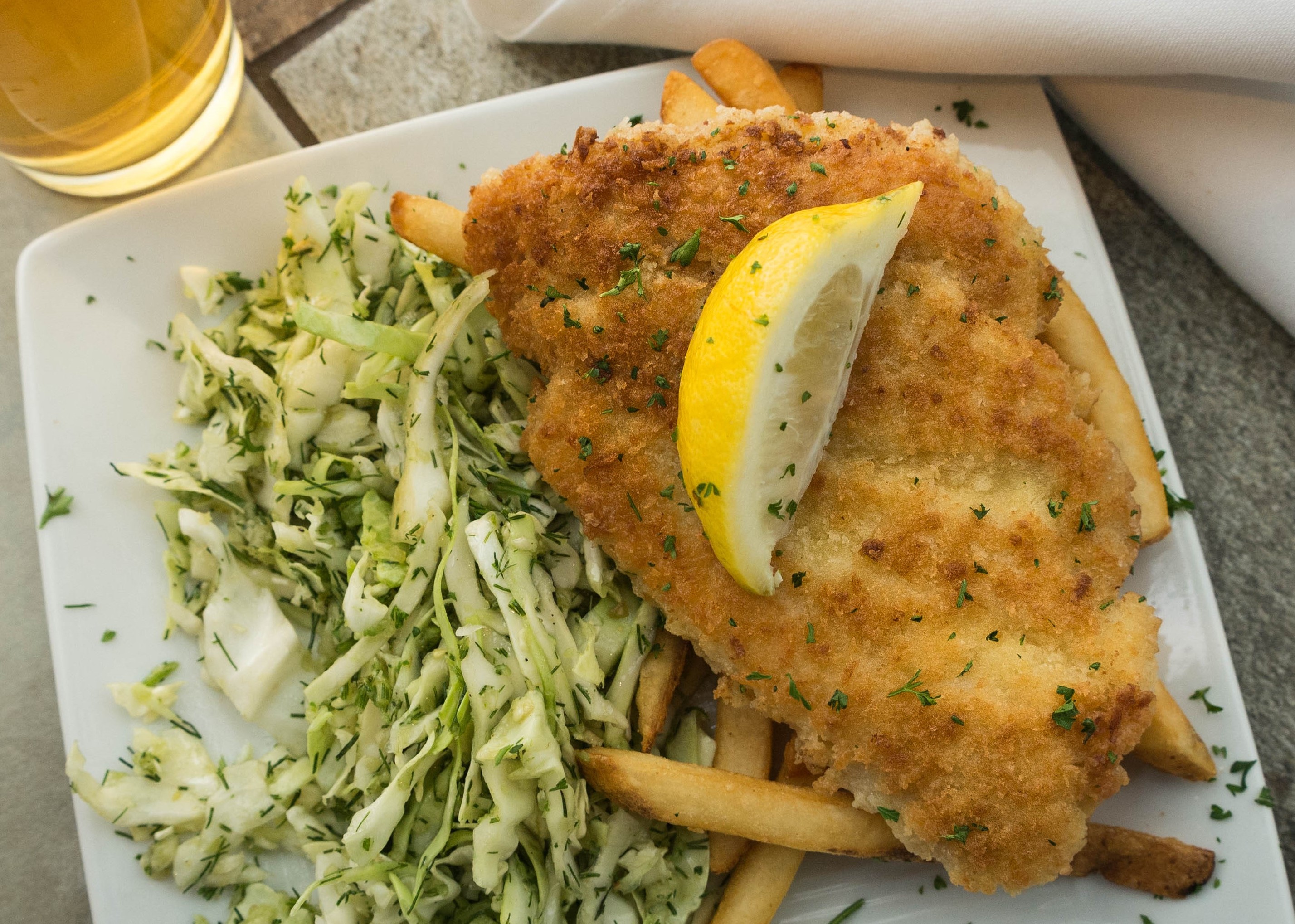 Panko-crusted fish with slaw and french fries garnished with a lemon.