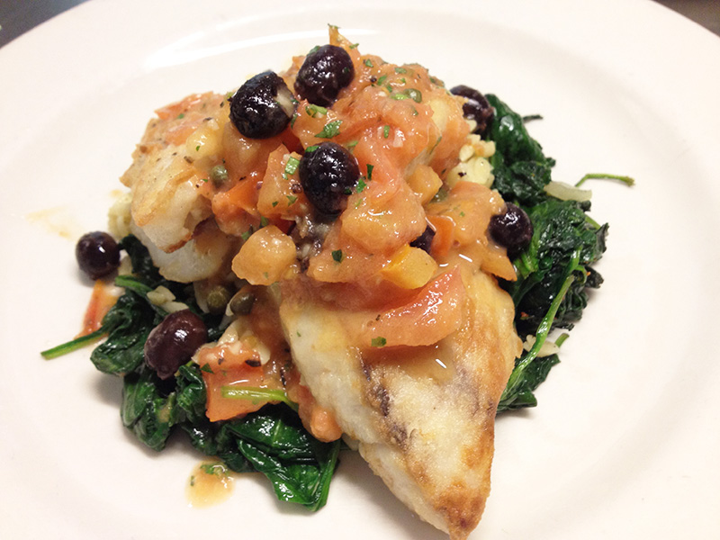 Dish with fish on spinach and black olive on top