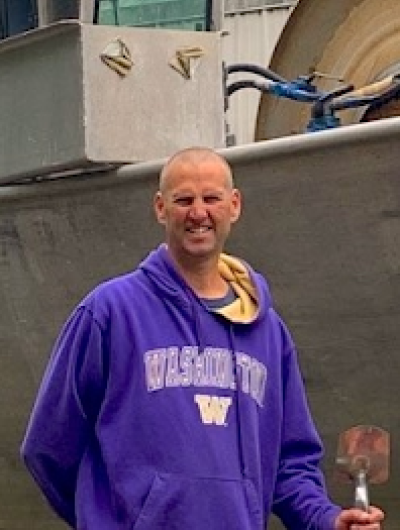 Andy Mitby of Drake Teal Fisheries stands in front of his boat in a University of Washington sweatshirt.