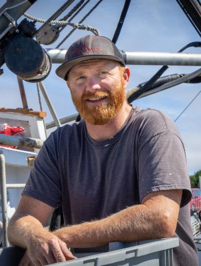 A fisherman with arms crossed, standing on the deck of a fishing boat