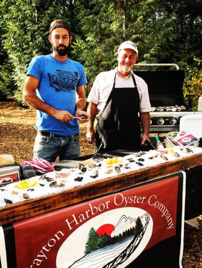Steve Seymour and his son, Mark Seymour pose shucking oysters behind a raw oyster bar stand for Drayton Harbor Oyster Company.