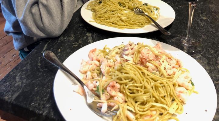 Two plates with spaghetti and shrimp on a dark table.