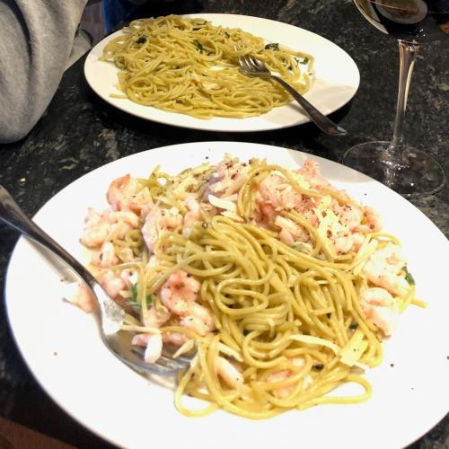 Two plates with spaghetti and shrimp on a dark table.